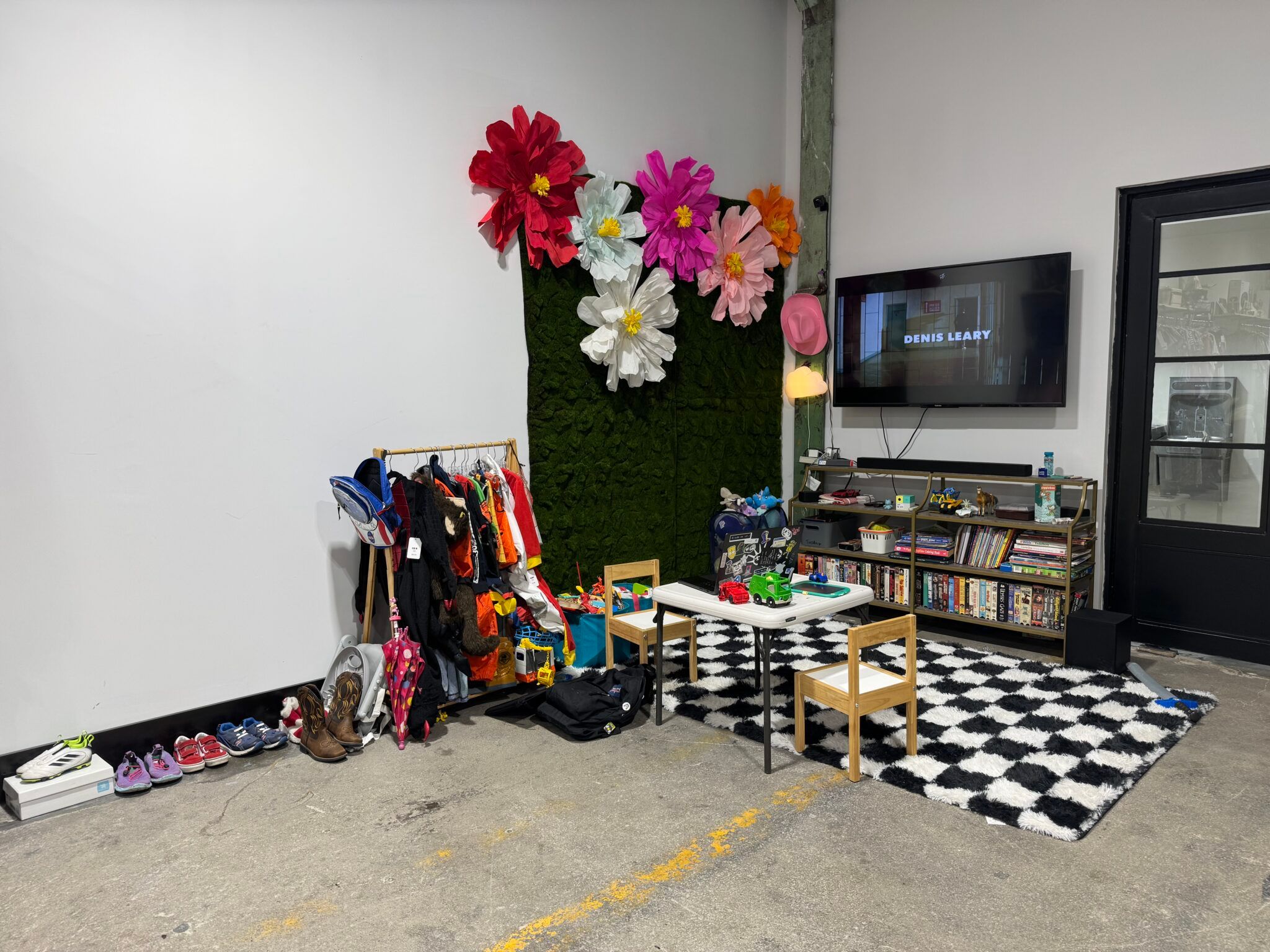 Inside Cliffhanger — a kids' corner with a paper-flower wall, a coat rack of children's costumes, a small play table, and donated shoes lined up along the floor.