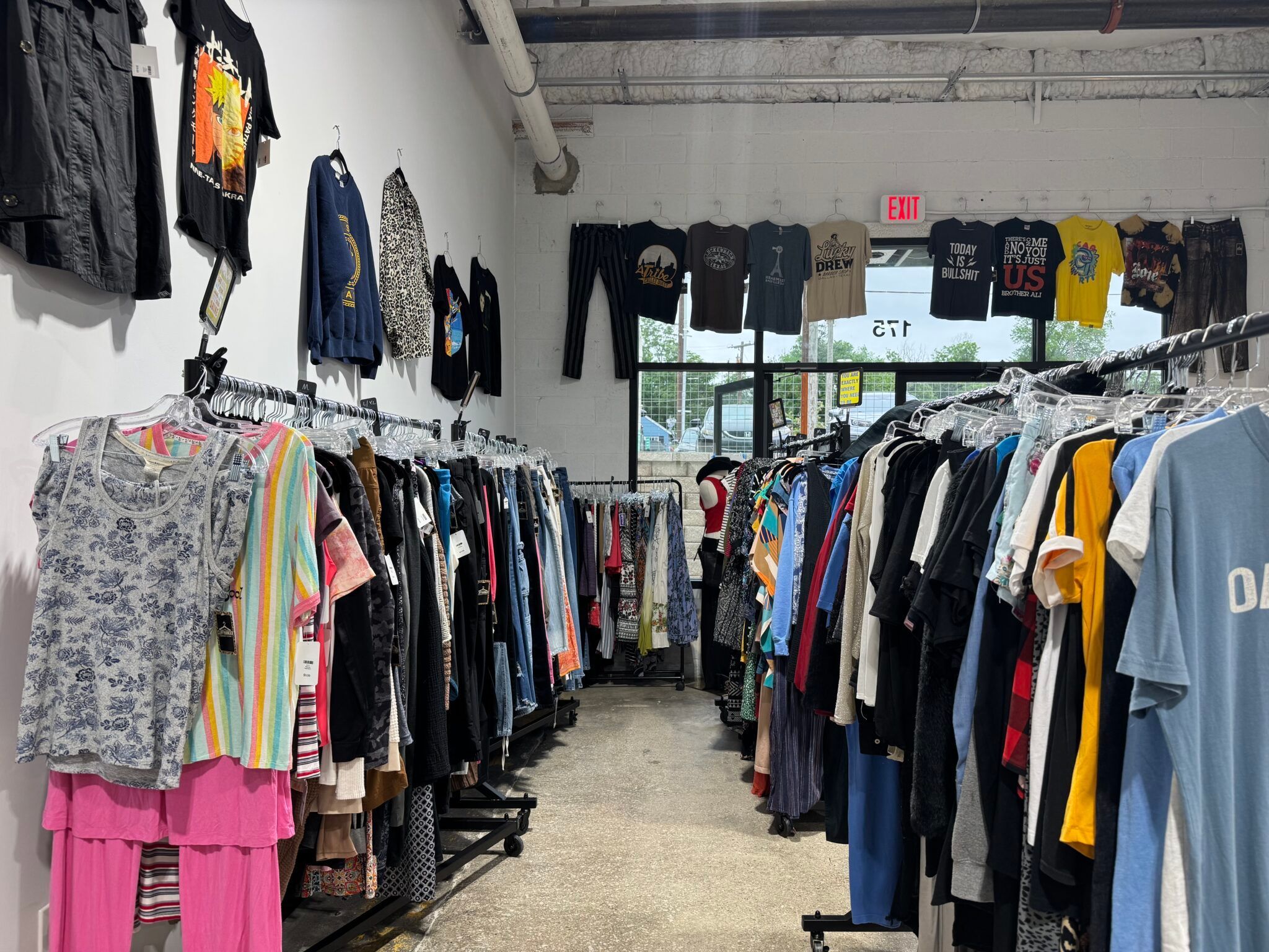 Inside Cliffhanger — clothing racks lining both sides of the aisle, with vintage tees taped above on the wall.